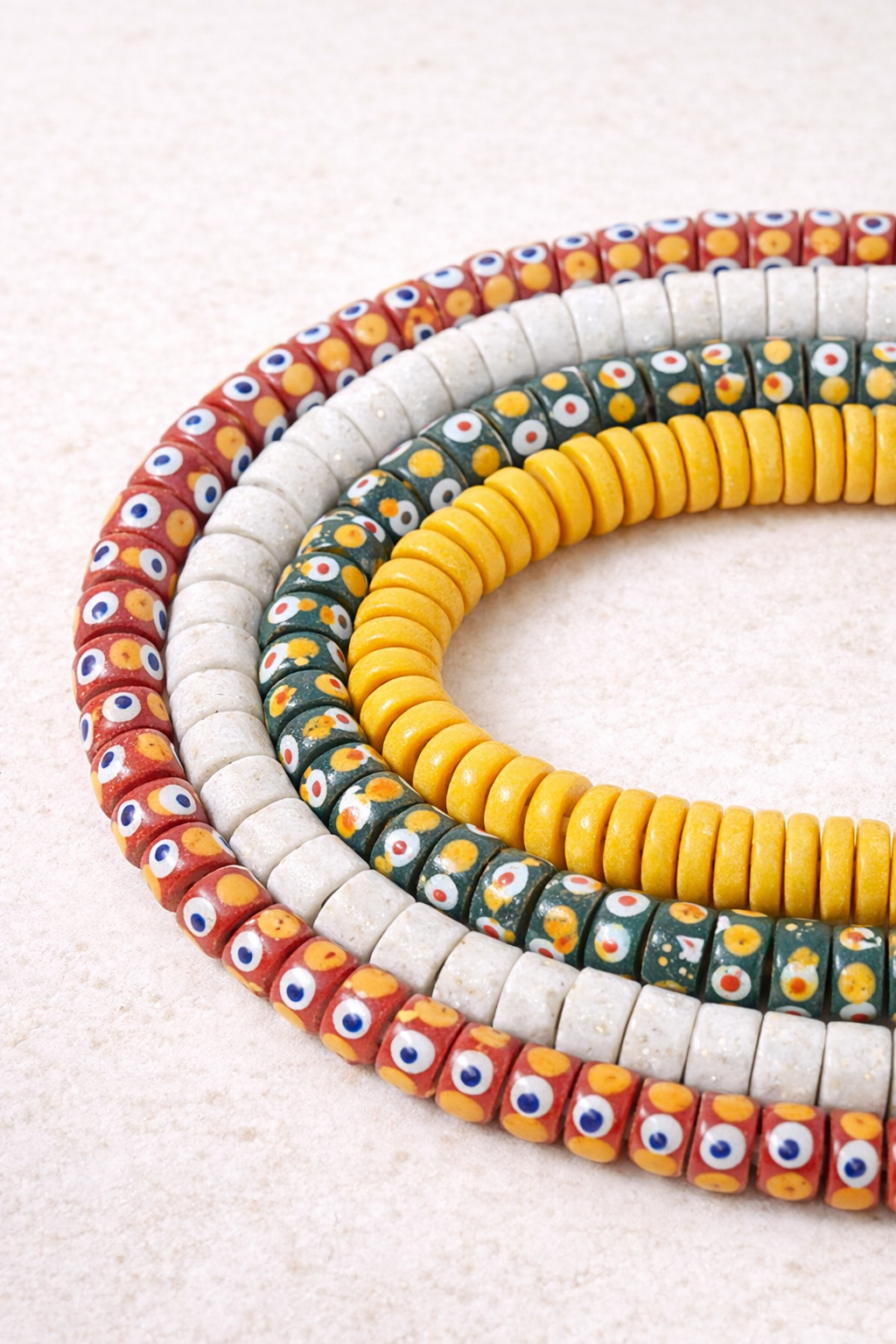 Handcrafted Ghanaian spacer glass beads arranged on an ivory background, highlighting uniform spacing and traditional beadmaking artistry.