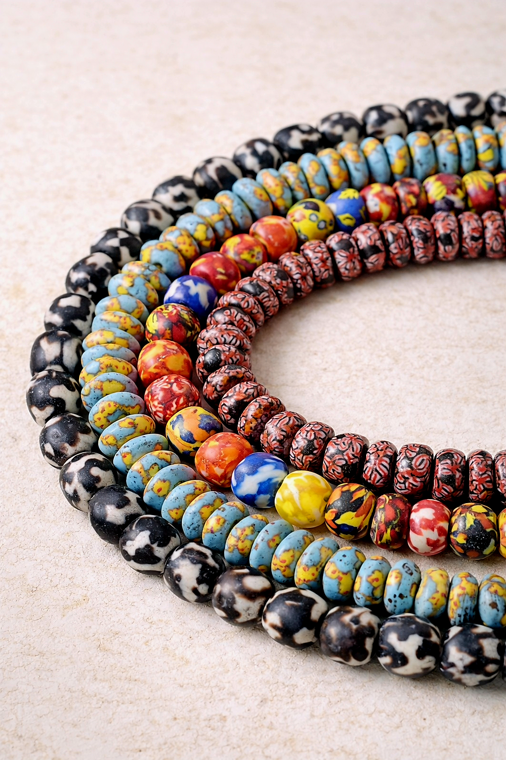 Handcrafted fused Krobo recycled glass beads from Ghana displayed on an ivory background, highlighting artisanal texture and traditional beadmaking techniques.