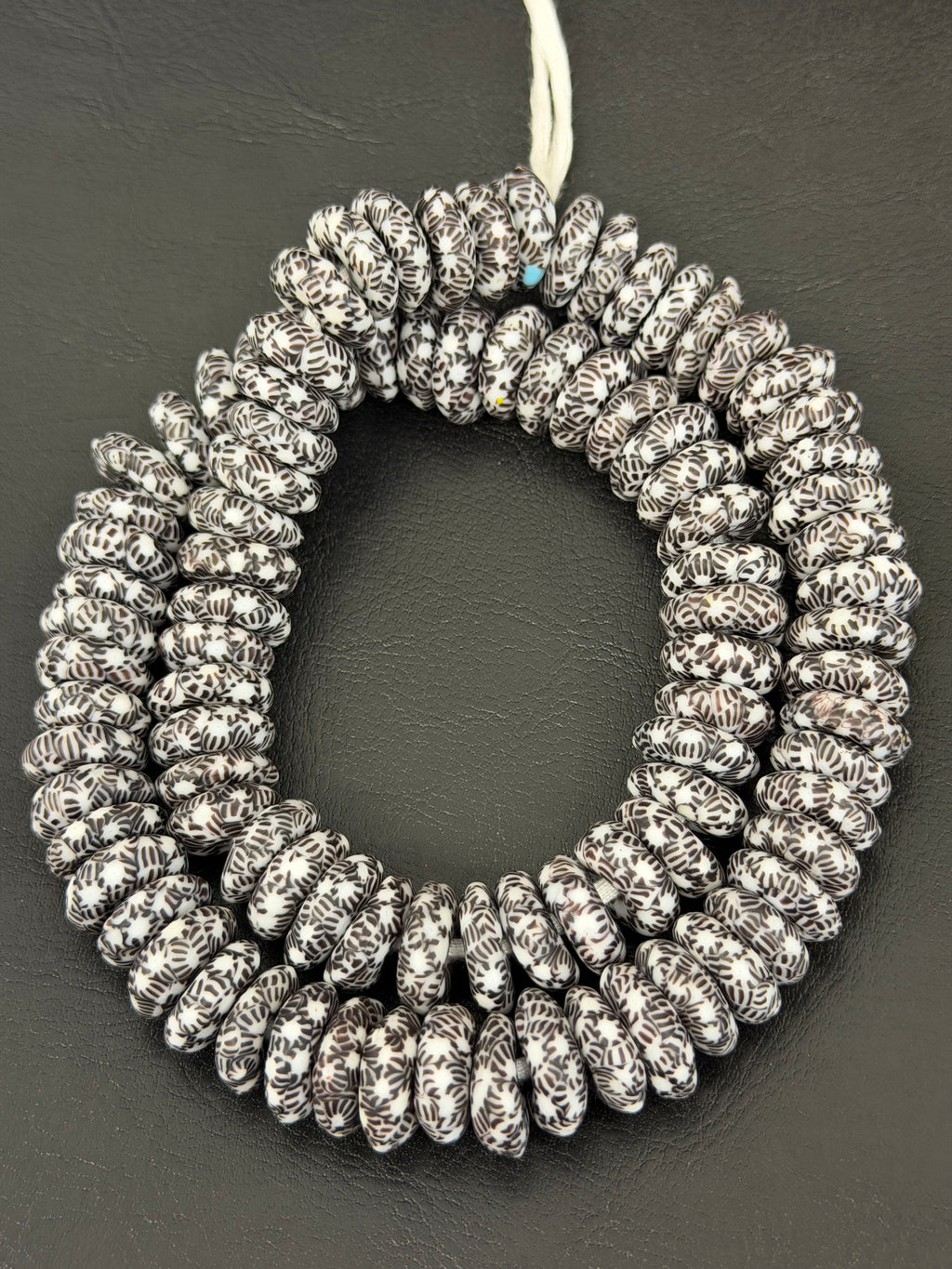 Authentic handcrafted black and white Fused Krobo Rondelle Recycled Glass Beads from Ghana featuring intricate artisan graphic patterns arranged as a full designer strand for luxury jewelry making and wholesale sourcing.