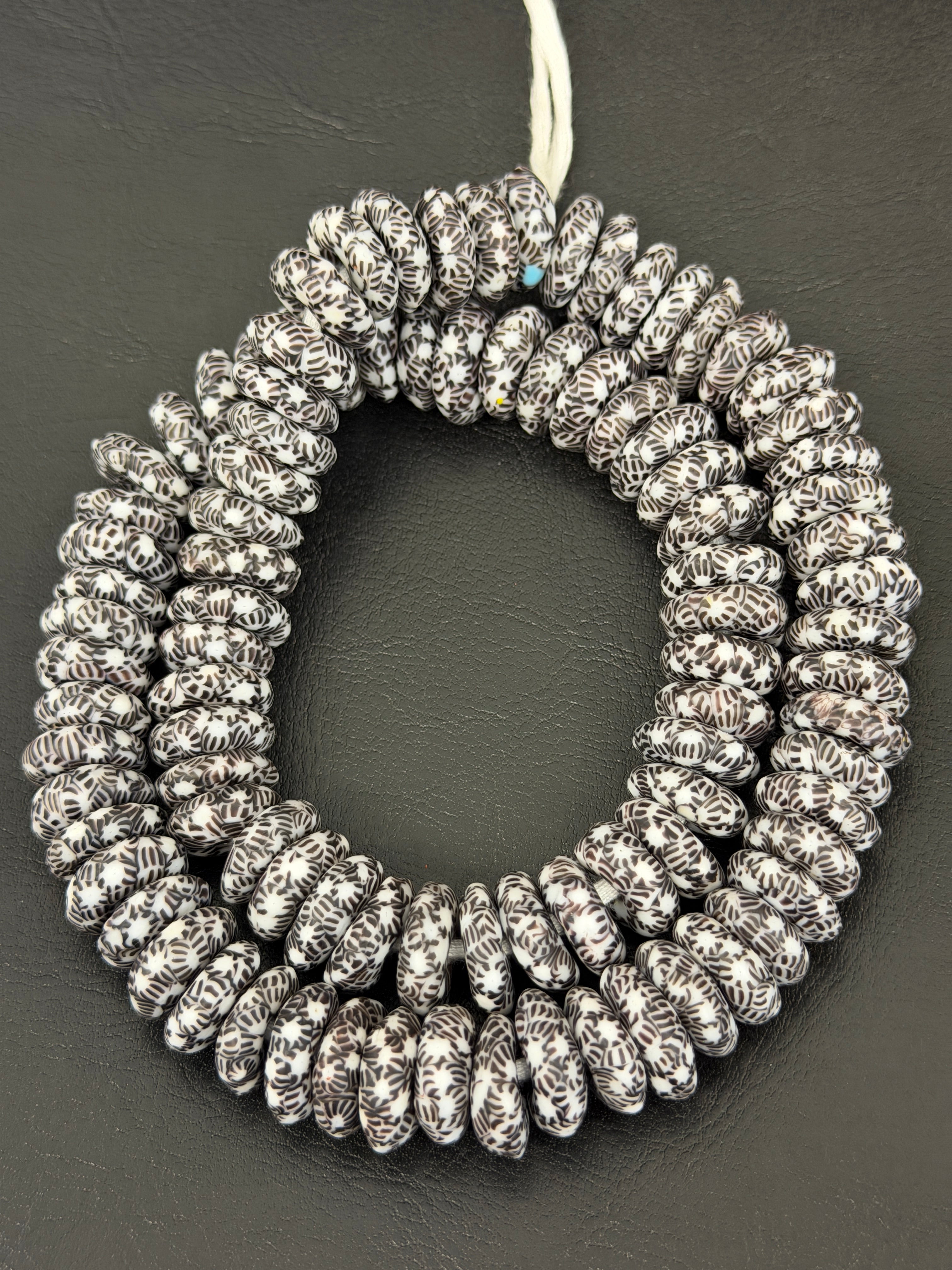 Authentic handcrafted black and white Fused Krobo Rondelle Recycled Glass Beads from Ghana featuring intricate artisan graphic patterns arranged as a full designer strand for luxury jewelry making and wholesale sourcing.