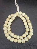 Authentic handcrafted ivory sand Krobo powdered glass beads from Ghana featuring organic round recycled glass beads with matte finish and warm natural artisan speckles arranged on a strand.