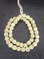 Authentic handcrafted ivory sand Krobo powdered glass beads from Ghana featuring organic round recycled glass beads with matte finish and warm natural artisan speckles arranged on a strand.