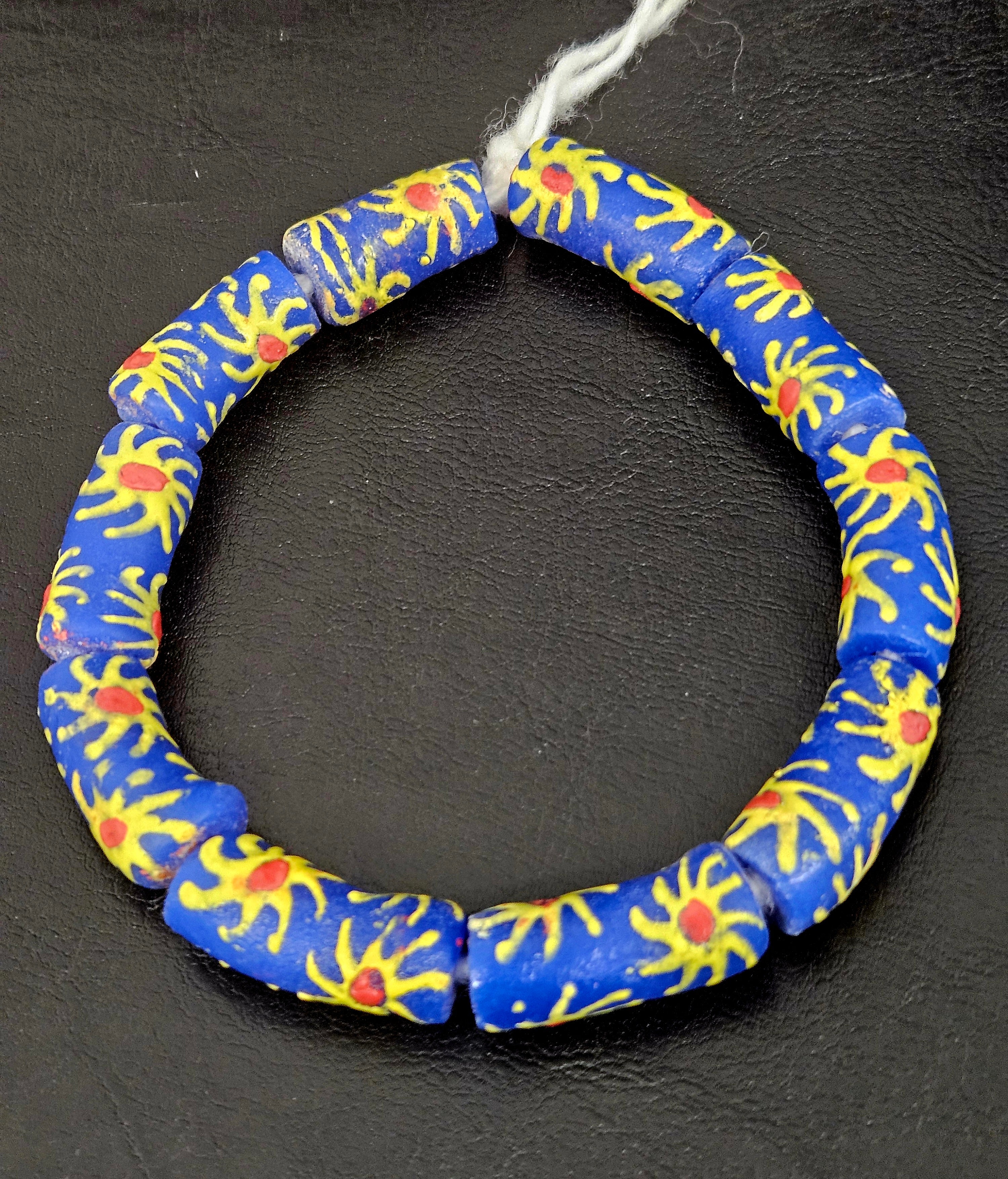 Authentic Painted Krobo Glass Tube Beads handcrafted in Ghana featuring matte royal blue recycled glass tube beads decorated with hand-painted golden yellow sunburst motifs and terracotta red accents for statement jewelry and artisan design.