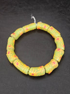 Authentic Painted Krobo Glass Tube Beads handcrafted in Ghana featuring matte sage green recycled glass tube beads decorated with hand-painted golden yellow sunburst motifs and terracotta red accents for statement jewelry and artisan design.