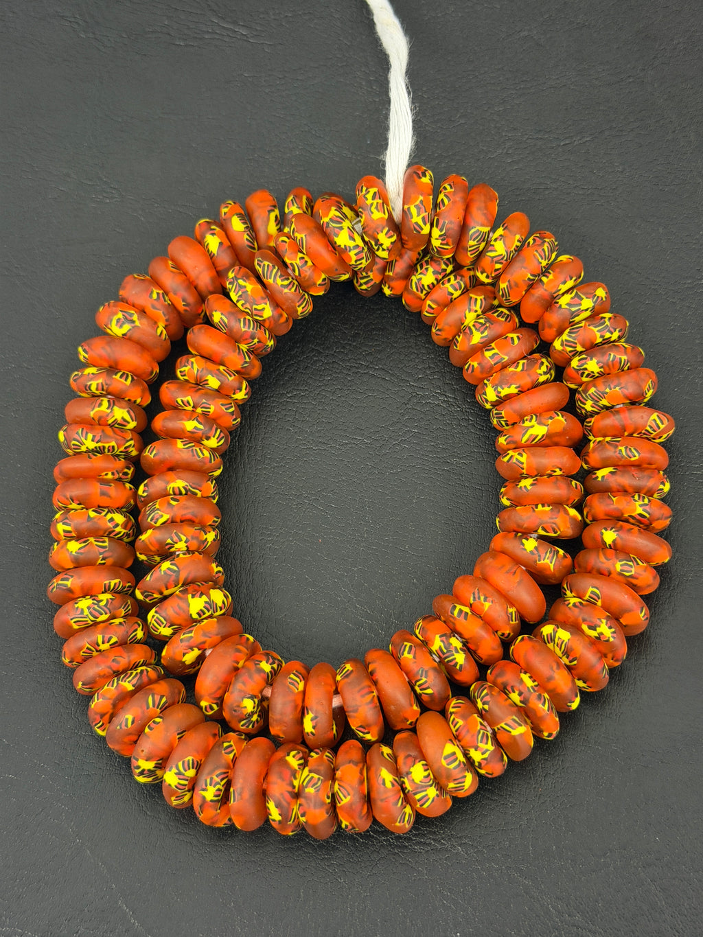 Authentic handcrafted rust orange Fused Krobo Rondelle Recycled Glass Beads from Ghana featuring golden yellow and charcoal artisan patterns arranged as a full strand for luxury jewelry making and wholesale designer sourcing.