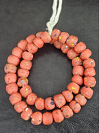 Authentic handcrafted terracotta red Krobo powdered glass beads from Ghana featuring organic round recycled glass beads with matte finish and colorful artisan inclusions arranged on a strand.