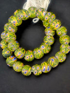 Strand of African trade beads sourced in Ghana featuring green and yellow glass beads with multicolored eye motifs, approximately 15–16mm with large 7–8mm holes for jewelry making and collectin