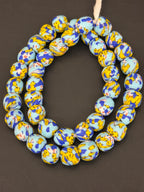 Authentic Fused Krobo recycled glass beads handcrafted in Ghana featuring sky blue, royal blue, golden yellow, and ivory fused patterns on approximately 44 artisan-made beads strung on a strand.