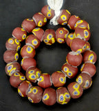 Strand of chocolate brown African trade beads sourced in Ghana featuring yellow eye motifs with blue, white, and black starburst centers, approximately 15–16mm with large 7–8mm holes for jewelry making and collecting.