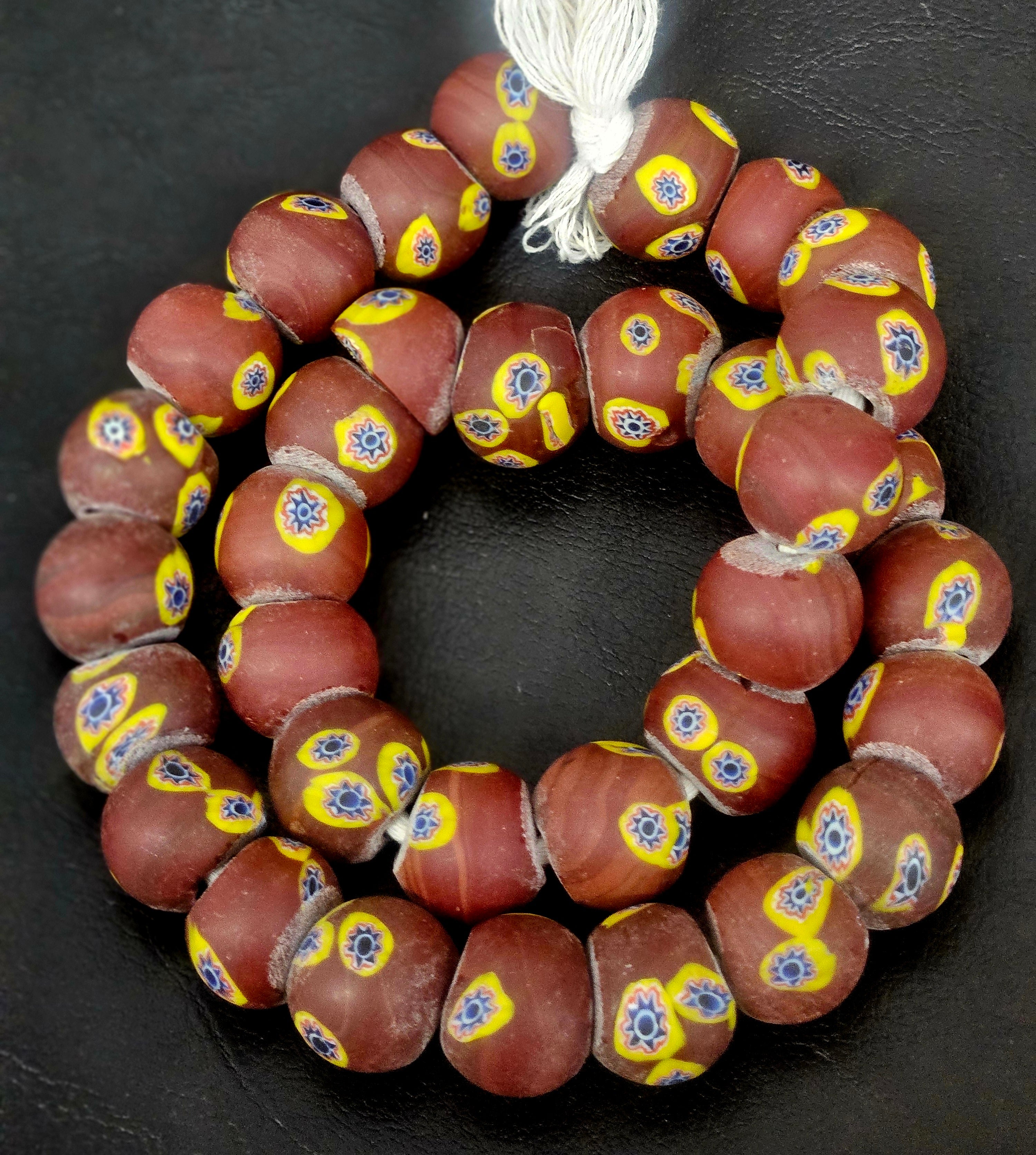 Strand of chocolate brown African trade beads sourced in Ghana featuring yellow eye motifs with blue, white, and black starburst centers, approximately 15–16mm with large 7–8mm holes for jewelry making and collecting.