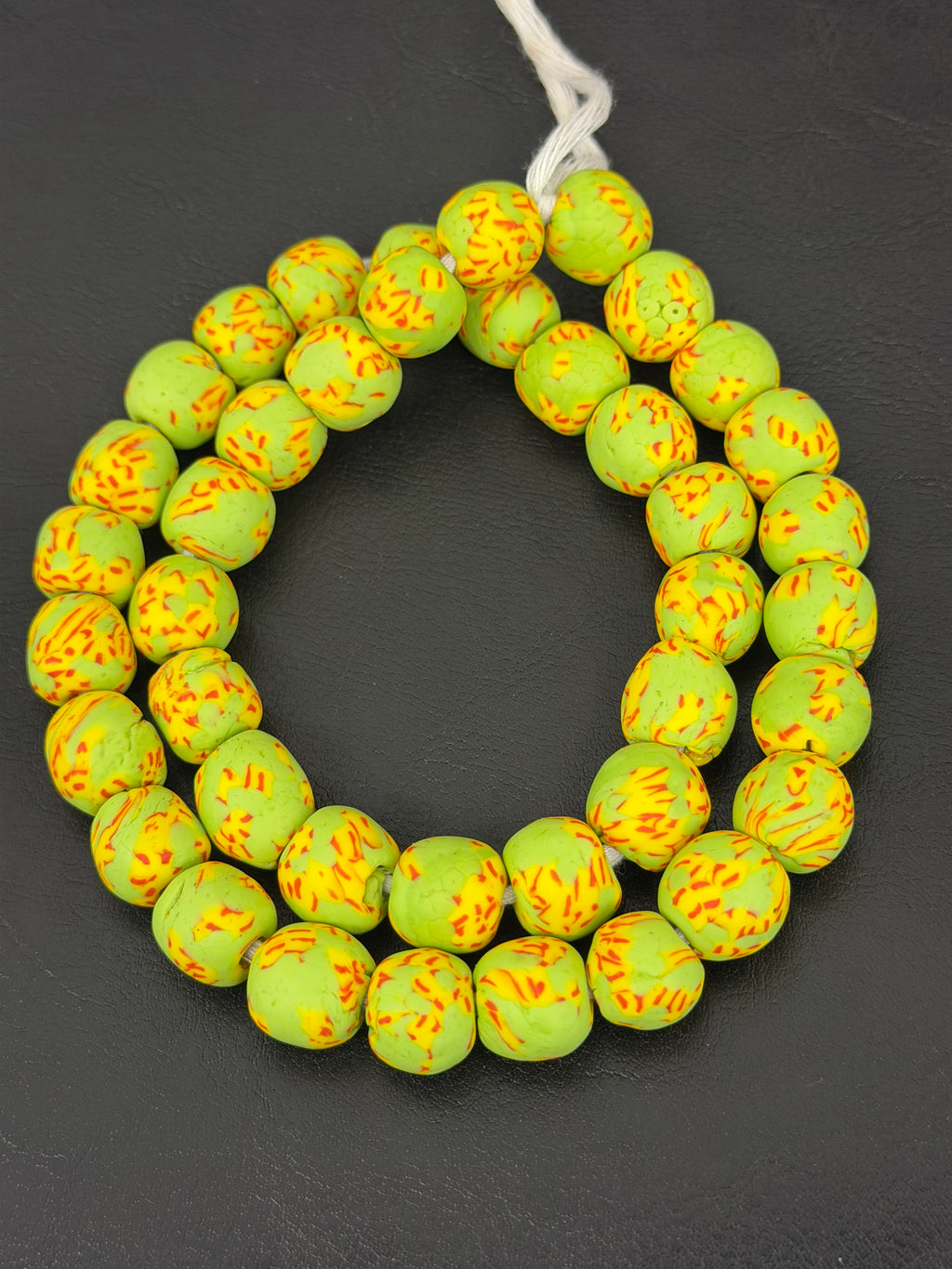 Authentic Fused Krobo recycled glass beads handcrafted in Ghana featuring lime green, golden yellow, and orange fused patterns on approximately 44 artisan-made beads strung on a strand.