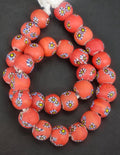 Strand of coral-orange African trade beads sourced in Ghana featuring yellow-centered eye motifs with blue, white, and black accents, approximately 15–16mm with large 7–8mm holes for jewelry making and collecting.