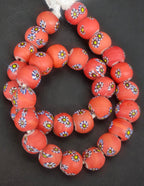 Strand of coral-orange African trade beads sourced in Ghana featuring yellow-centered eye motifs with blue, white, and black accents, approximately 15–16mm with large 7–8mm holes for jewelry making and collecting.