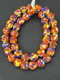 Authentic Fused Krobo recycled glass beads handcrafted in Ghana featuring coral red, royal blue, golden yellow, ivory, and earth-toned mosaic fused patterns on approximately 44 artisan-made beads strung on a strand.