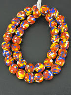 Authentic Fused Krobo recycled glass beads handcrafted in Ghana featuring coral red, royal blue, golden yellow, ivory, and earth-toned mosaic fused patterns on approximately 44 artisan-made beads strung on a strand.