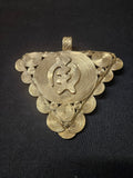 Oversized Gye Nyame Adinkra brass pendant from Ghana with triangular form, central symbol, concentric rings, and spiral decoration.