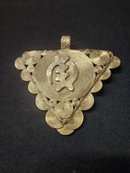 Oversized Gye Nyame Adinkra brass pendant from Ghana with triangular form, central symbol, concentric rings, and spiral decoration.