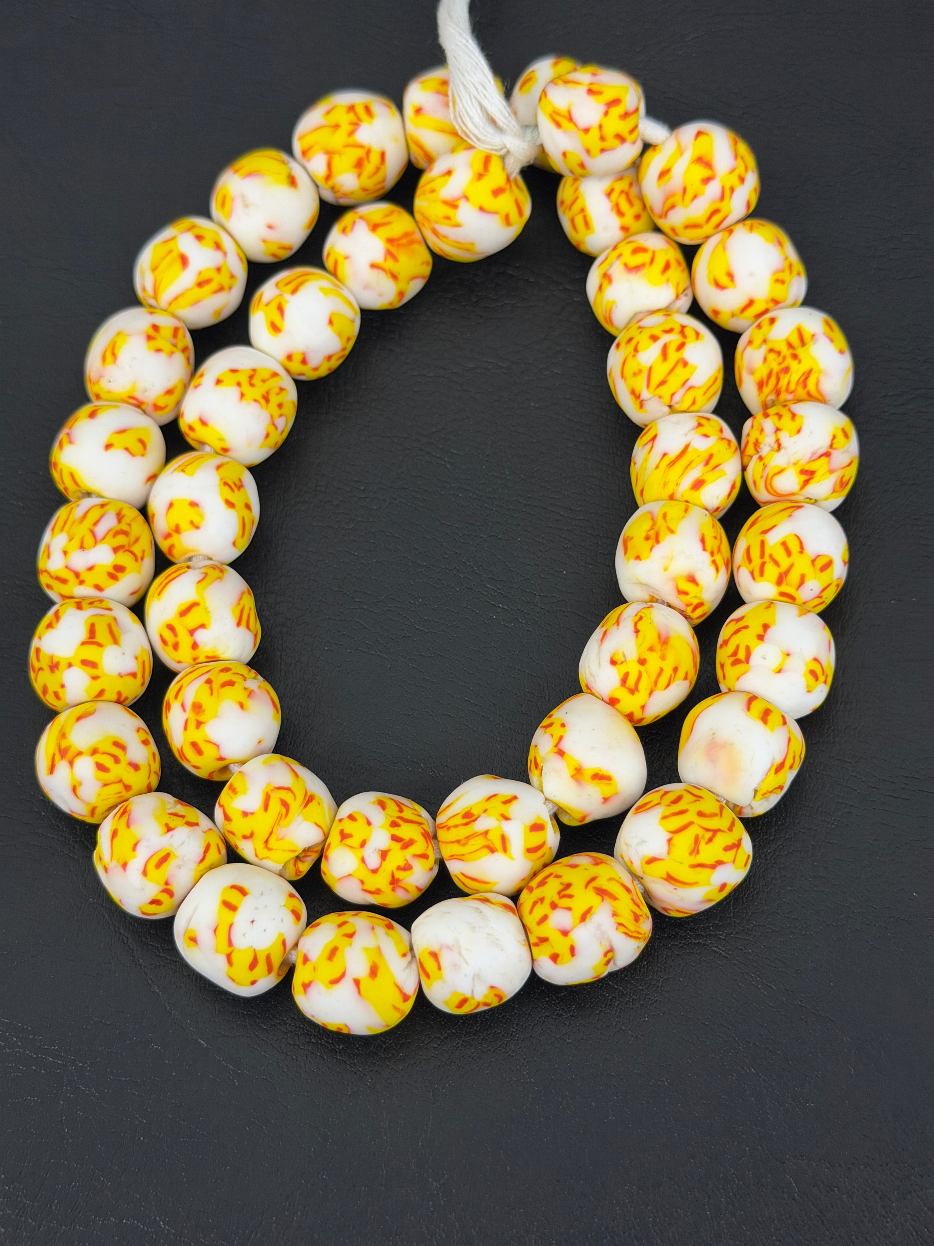 Authentic Fused Krobo recycled glass beads handcrafted in Ghana featuring ivory, golden yellow, and tangerine fused patterns on approximately 44 artisan-made beads strung on a strand.