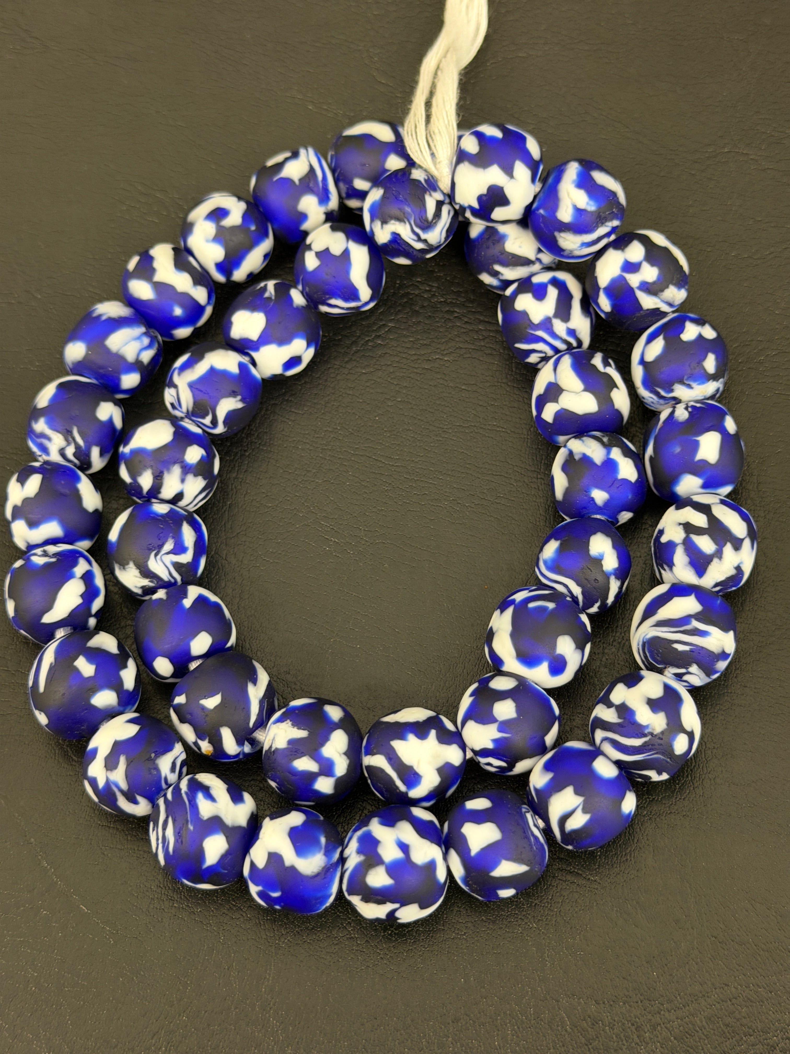 Authentic Fused Krobo recycled glass beads handcrafted in Ghana featuring cobalt blue, ivory white, and black fused patterns on approximately 44 artisan-made beads strung on a strand.