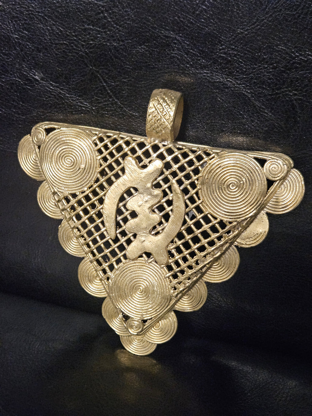 Side view of oversized African brass pendant showing its dimensional handcrafted construction and raised decorative elements.