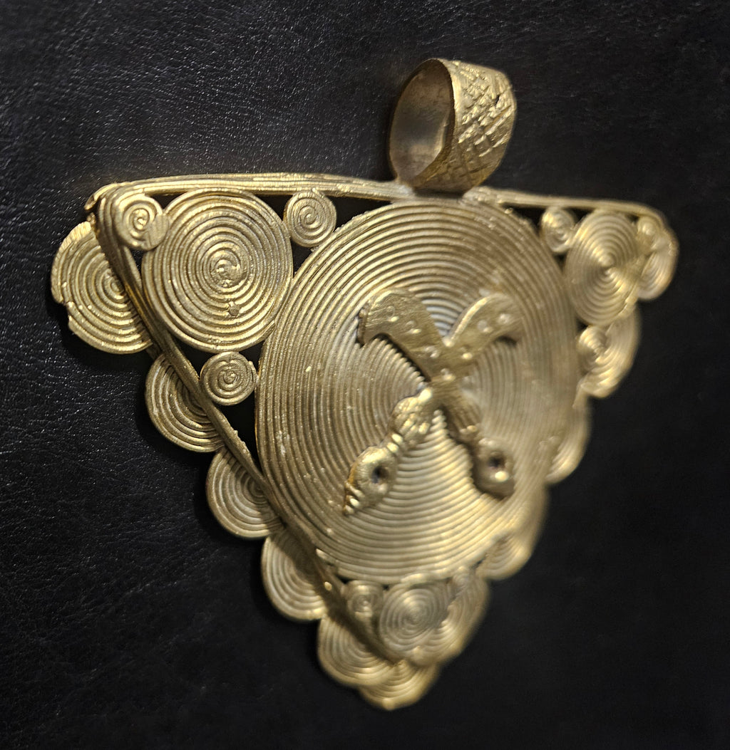 Angled view of oversized Akofena brass pendant showing dimensional relief and handcrafted surface texture.