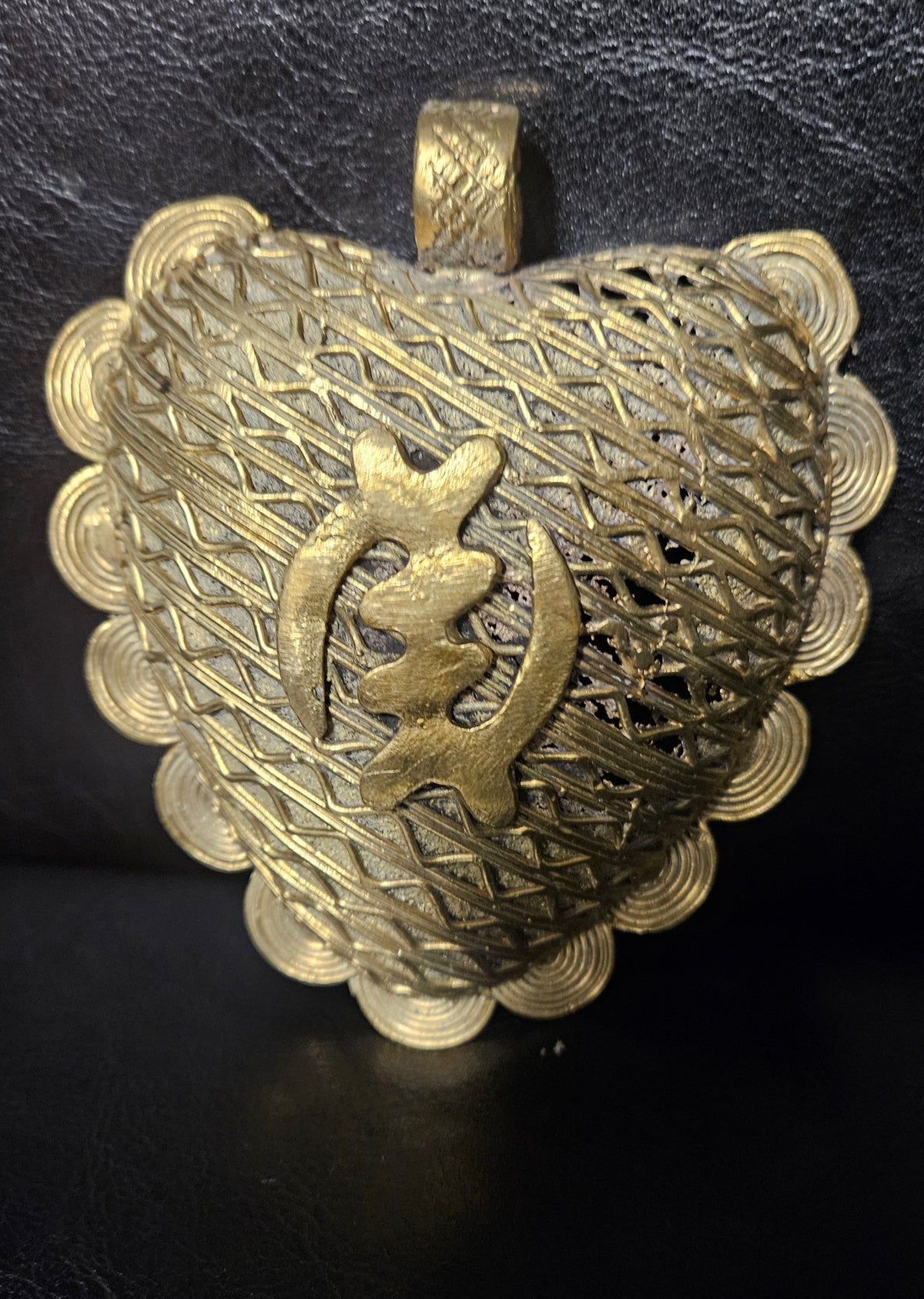 Oversized Gye Nyame Adinkra brass pendant from Ghana with central symbol, layered linear detailing, spiral border elements, and large bail.