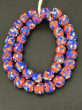 Authentic Fused Krobo recycled glass beads handcrafted in Ghana featuring coral red, royal blue, ivory, and black fused patterns on approximately 44 artisan-made beads strung on a strand.