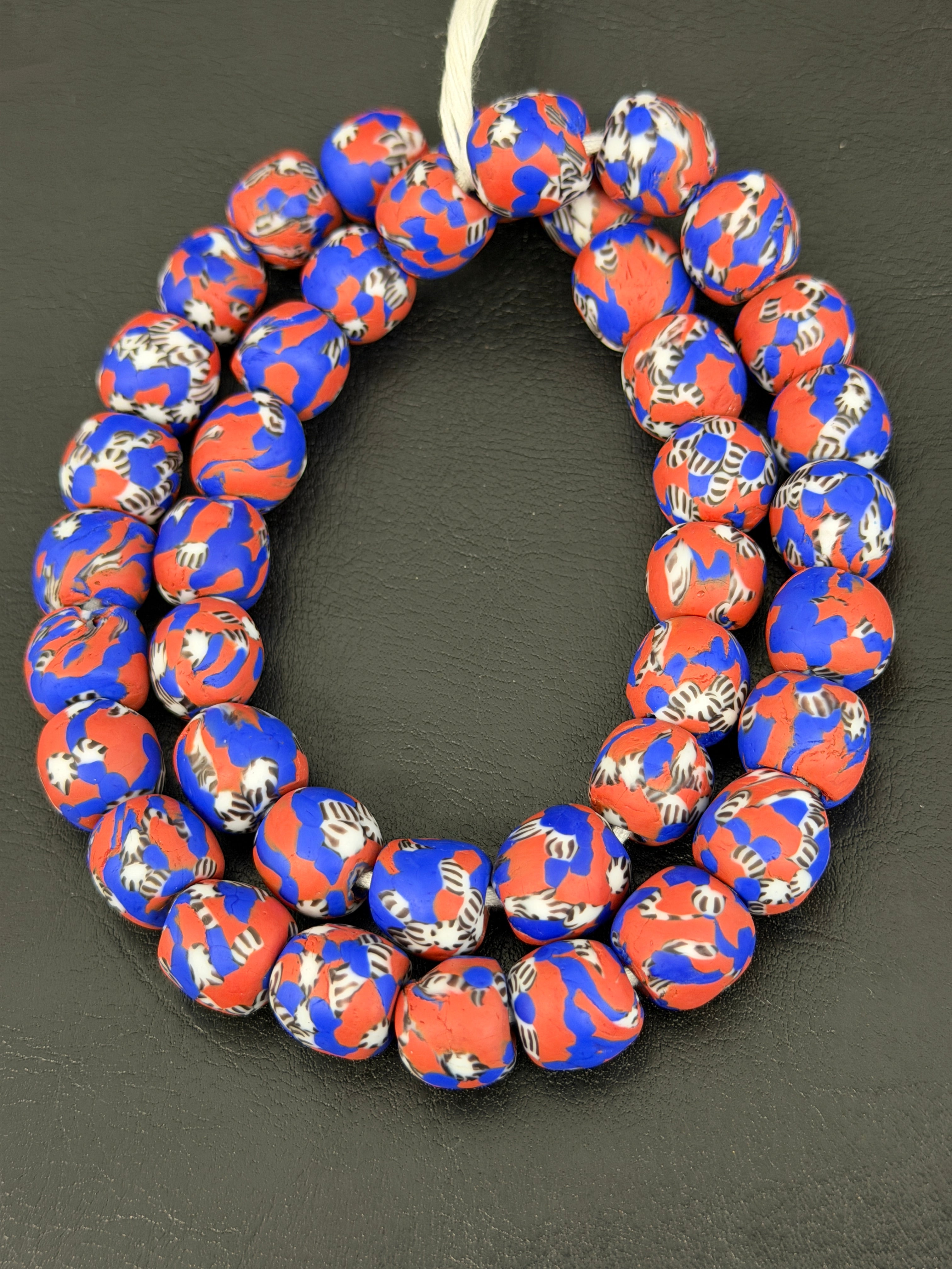 Authentic Fused Krobo recycled glass beads handcrafted in Ghana featuring coral red, royal blue, ivory, and black fused patterns on approximately 44 artisan-made beads strung on a strand.