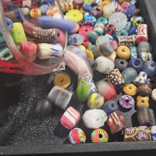 Video of assorted Krobo beads being poured into a black tray to display textures and colors.
