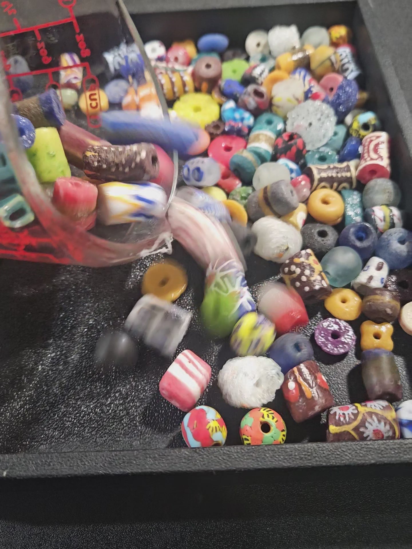 Video of assorted Krobo beads being poured into a black tray to display textures and colors.