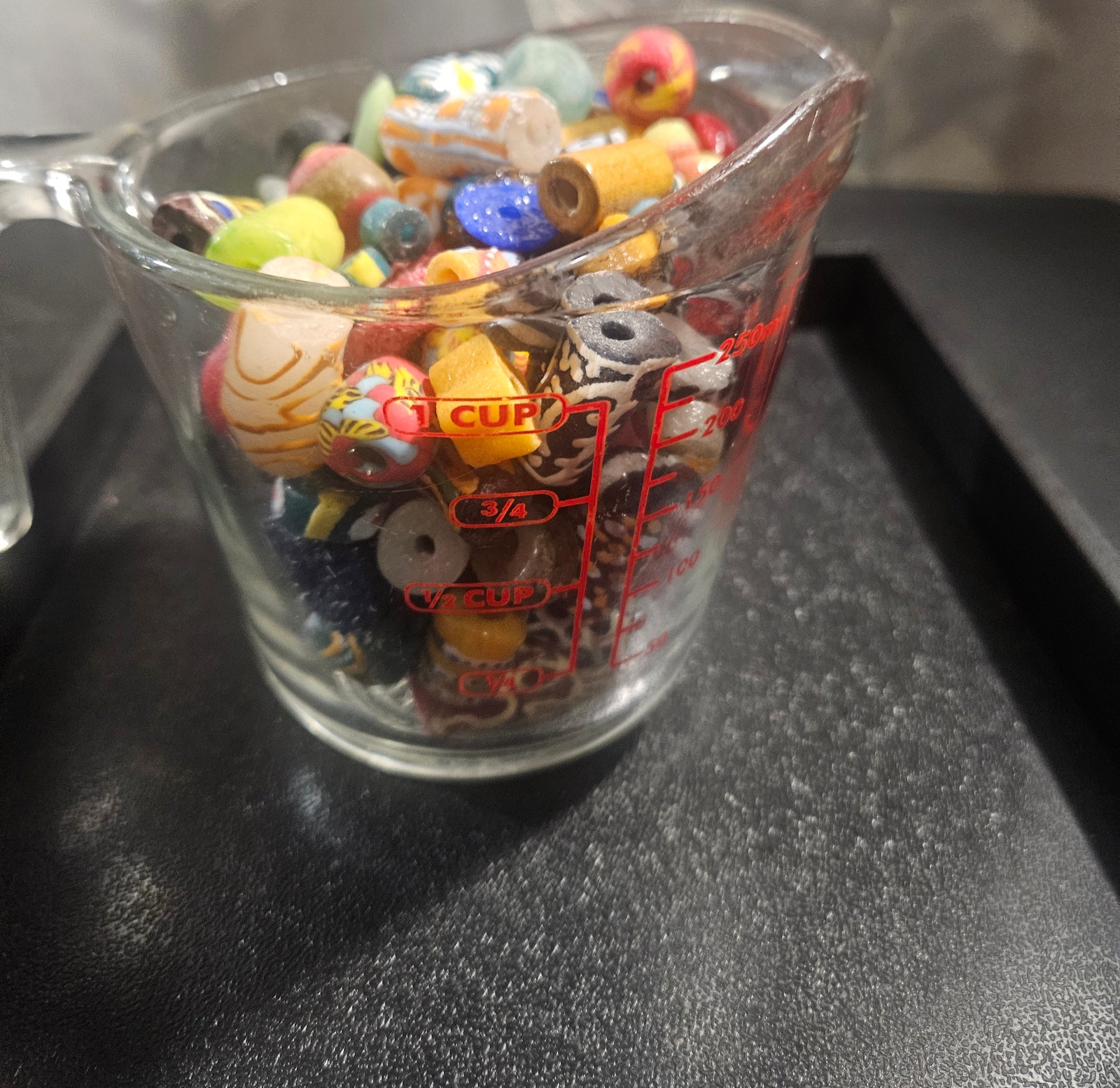 Measuring cup filled with jewel tone Krobo beads.