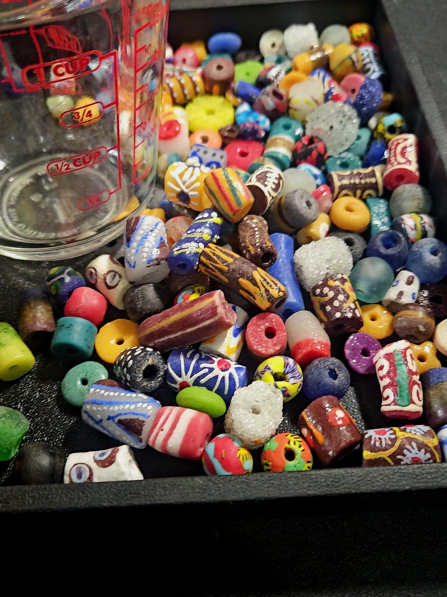 Lifestyle photo of assorted Krobo recycled glass beads inside a measuring cup.