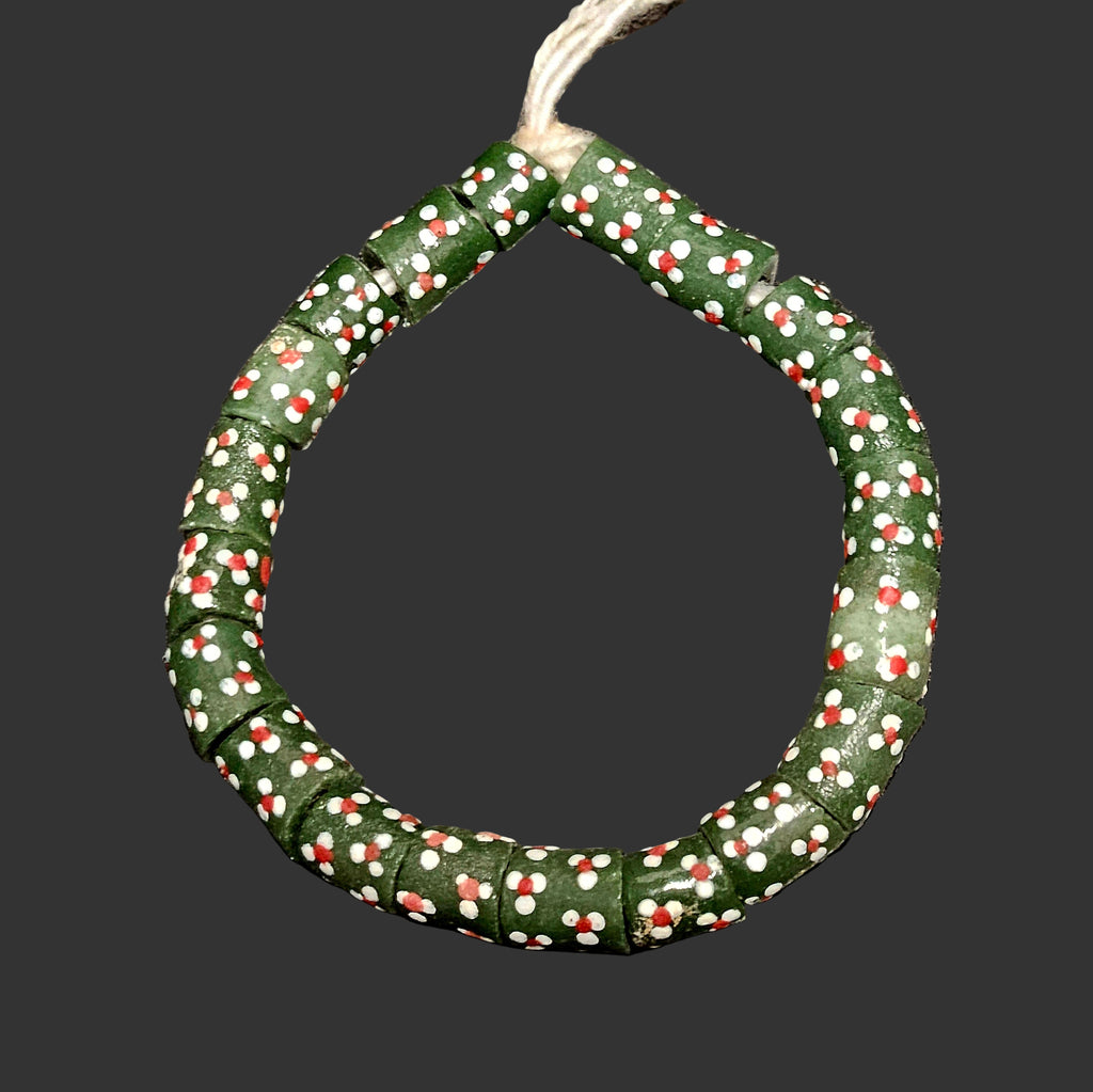 Green African recycled glass beads strand with white and red pattern on a dark textured background