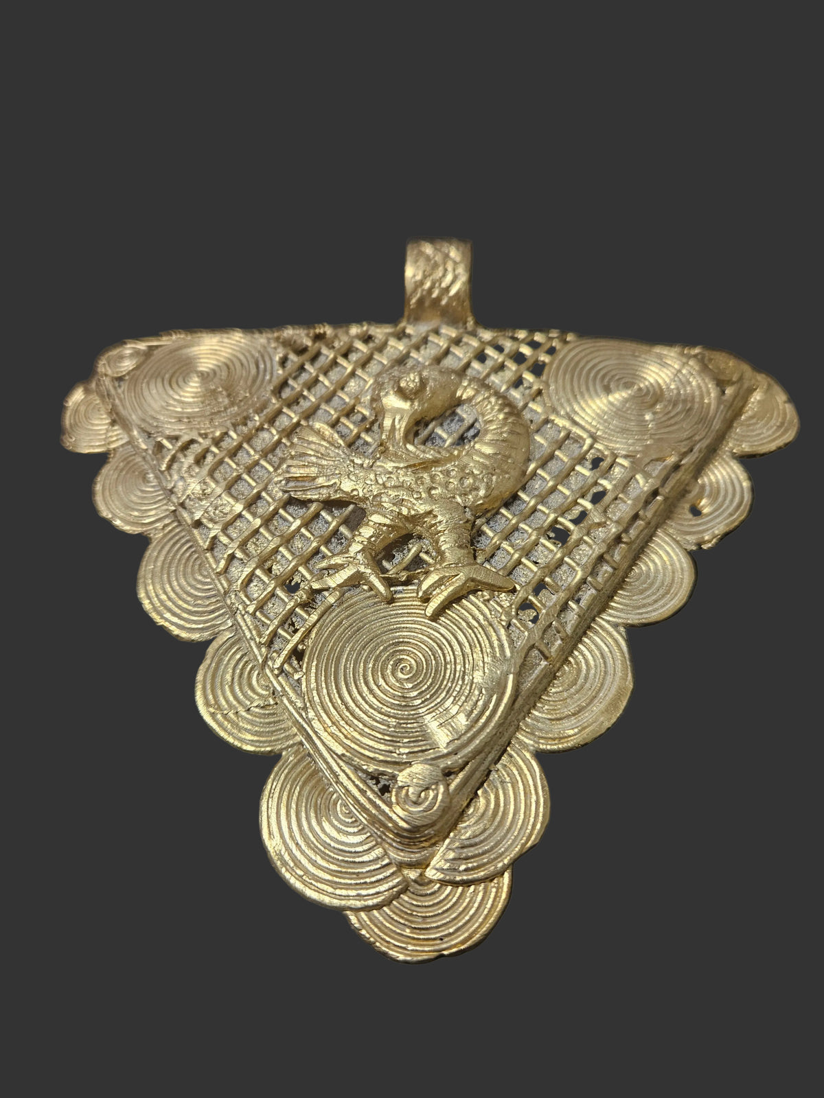 Front view of oversized Sankofa Bird Adinkra brass pendant from Ghana with triangular openwork design, spiral decoration, and large bail.