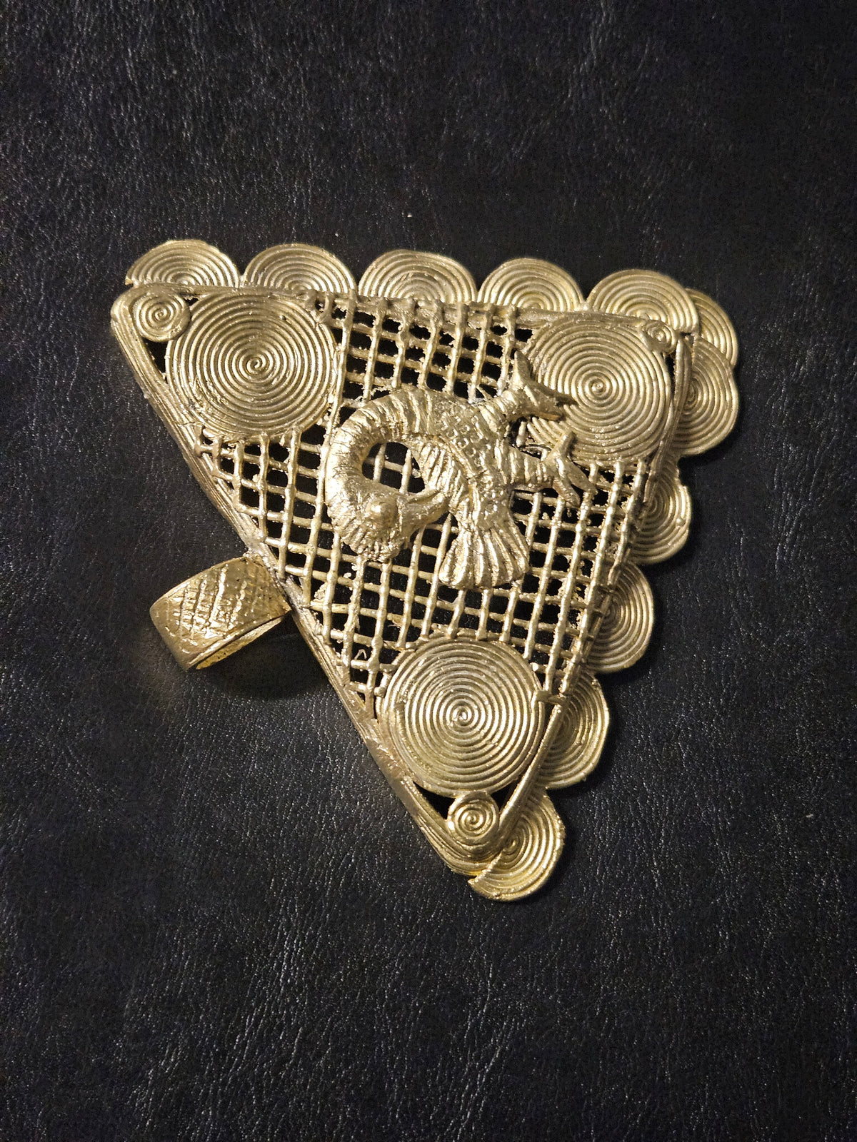 Close view of the wide textured brass bail on a handcrafted Sankofa Adinkra pendant from Ghana.