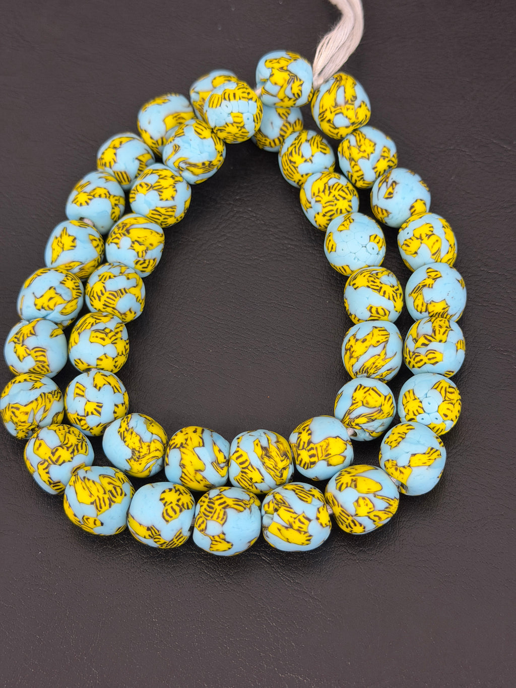 Authentic Fused Krobo recycled glass beads handcrafted in Ghana featuring sky blue and golden yellow fused patterns on approximately 44 artisan-made beads strung on a strand.
