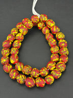 Authentic Fused Krobo recycled glass beads handcrafted in Ghana featuring crimson red, golden yellow, and black fused patterns on approximately 44 artisan-made beads strung on a strand.