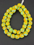 Authentic Fused Krobo recycled glass beads handcrafted in Ghana featuring pistachio green, sky blue, and golden yellow fused patterns on approximately 44 artisan-made beads strung on a strand.