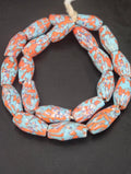Handcrafted XL orange fused Krobo recycled glass beads from Ghana featuring artisan ivory and charcoal patterns, approximately 12–14mm x 30–34mm.