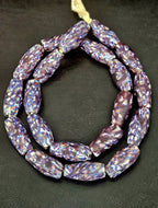 Handcrafted XL indigo fused Krobo recycled glass beads from Ghana featuring ivory, blue, and rust artisan patterning in elongated barrel shapes.